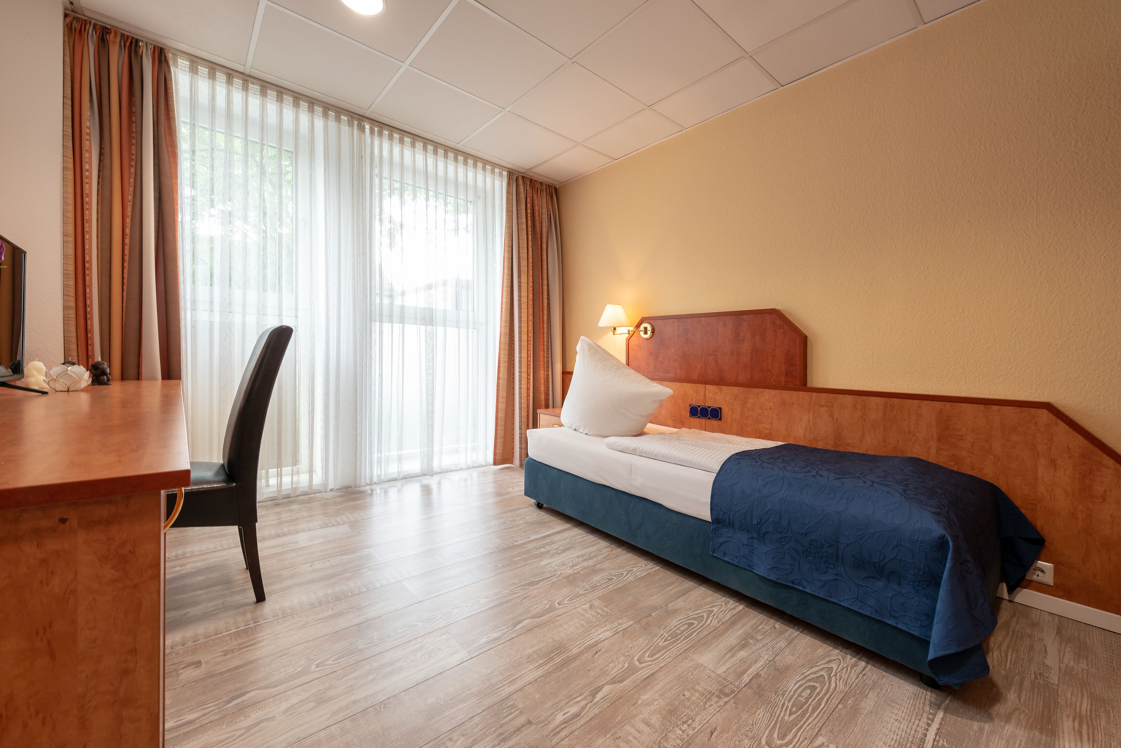 A hotel room with a bed, a desk, a chair, and a lamp.