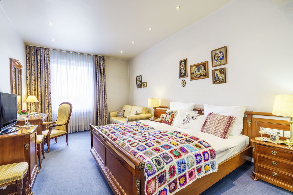 Une chambre d’hôtel avec un grand lit, un bureau avec une télévision, une chaise et une fenêtre avec des rideaux.
