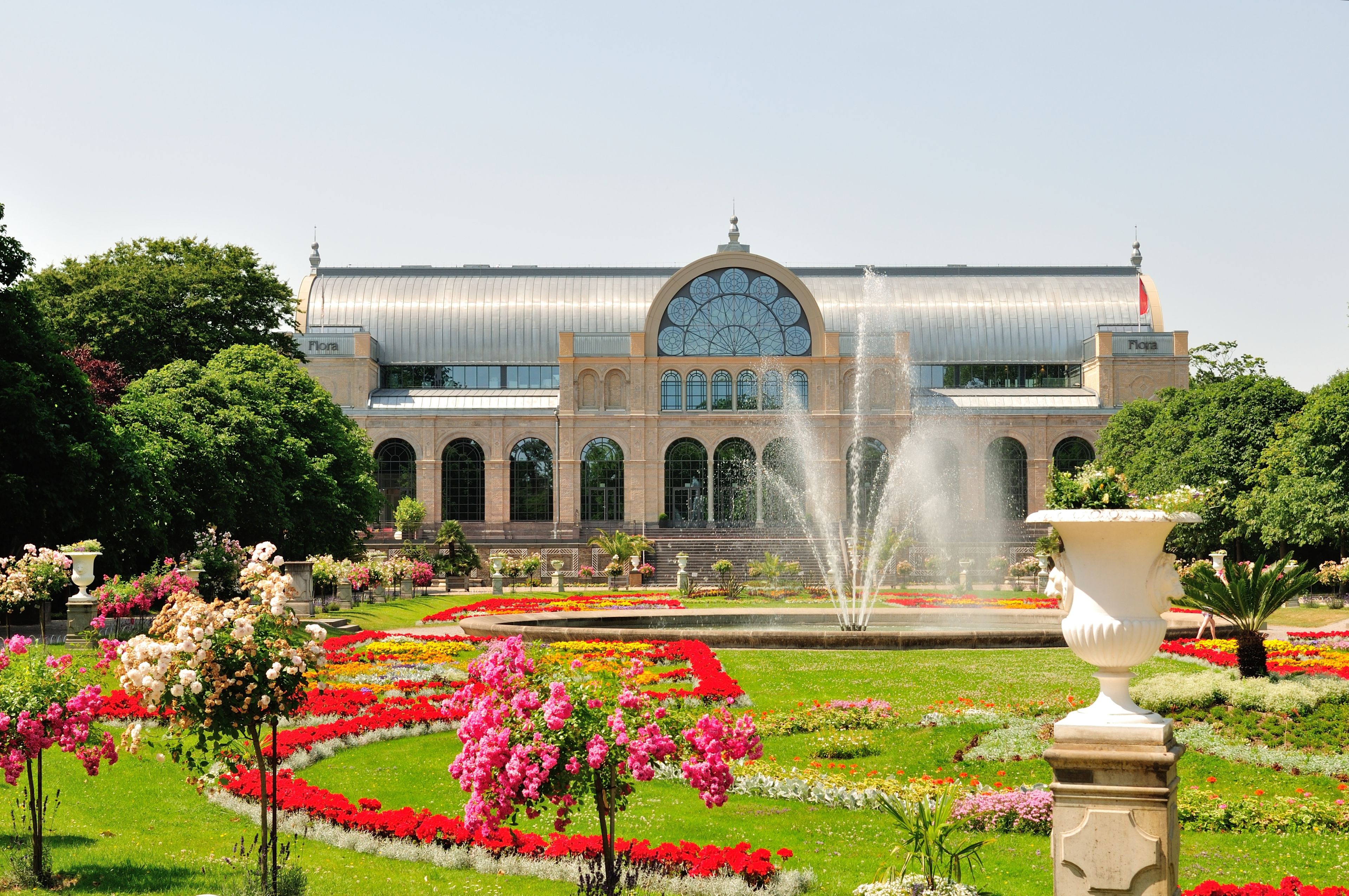 Un edificio grande con una cúpula y ventanas arqueadas, rodeado de un jardín bien cuidado con una fuente central.