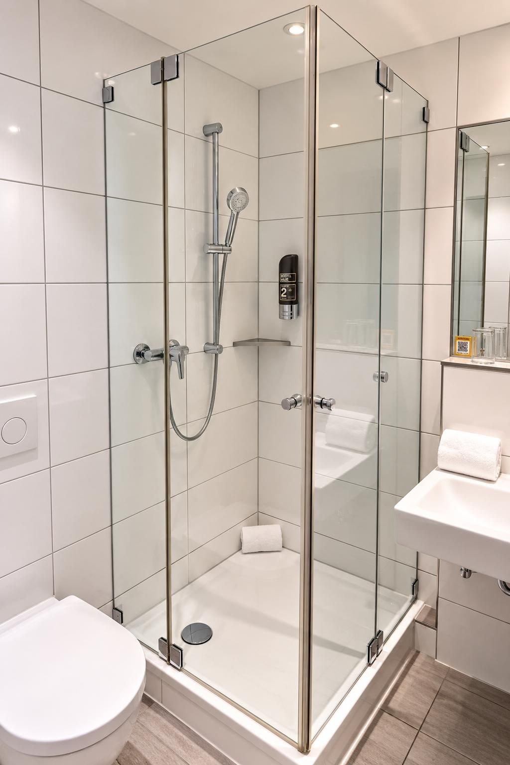 Ein modernes Badezimmer mit einer Duschkabine, einer weißen Toilette und einem Waschbecken mit Spiegel.