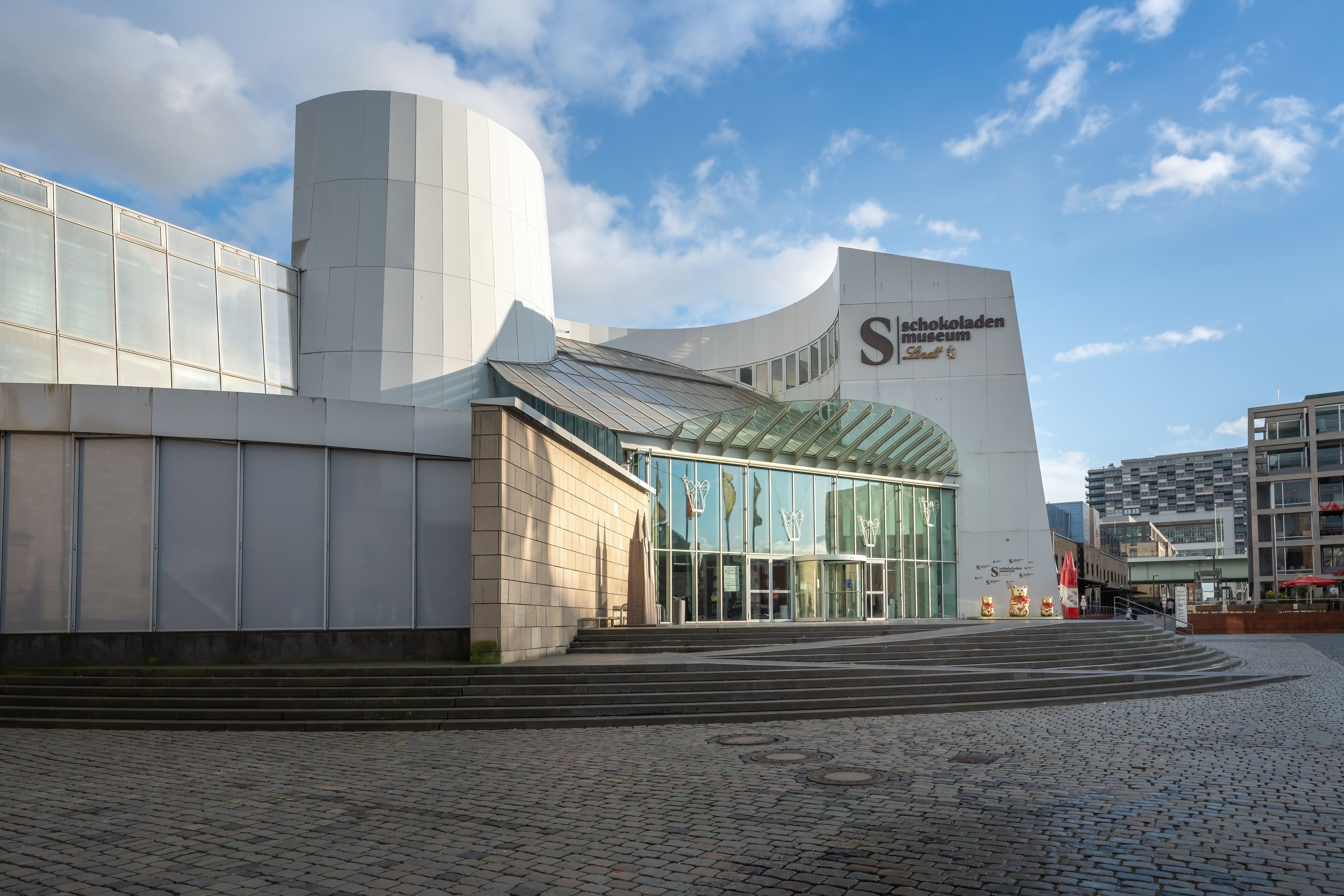 Een modern gebouw met een gebogen gevel, grote glasramen en een opvallend bord voor het Schokoladen Museum.