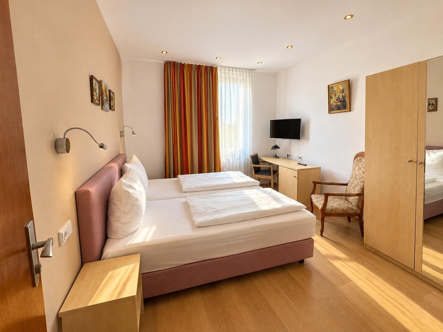 A hotel room with a bed, desk, chair, television, and a wardrobe.