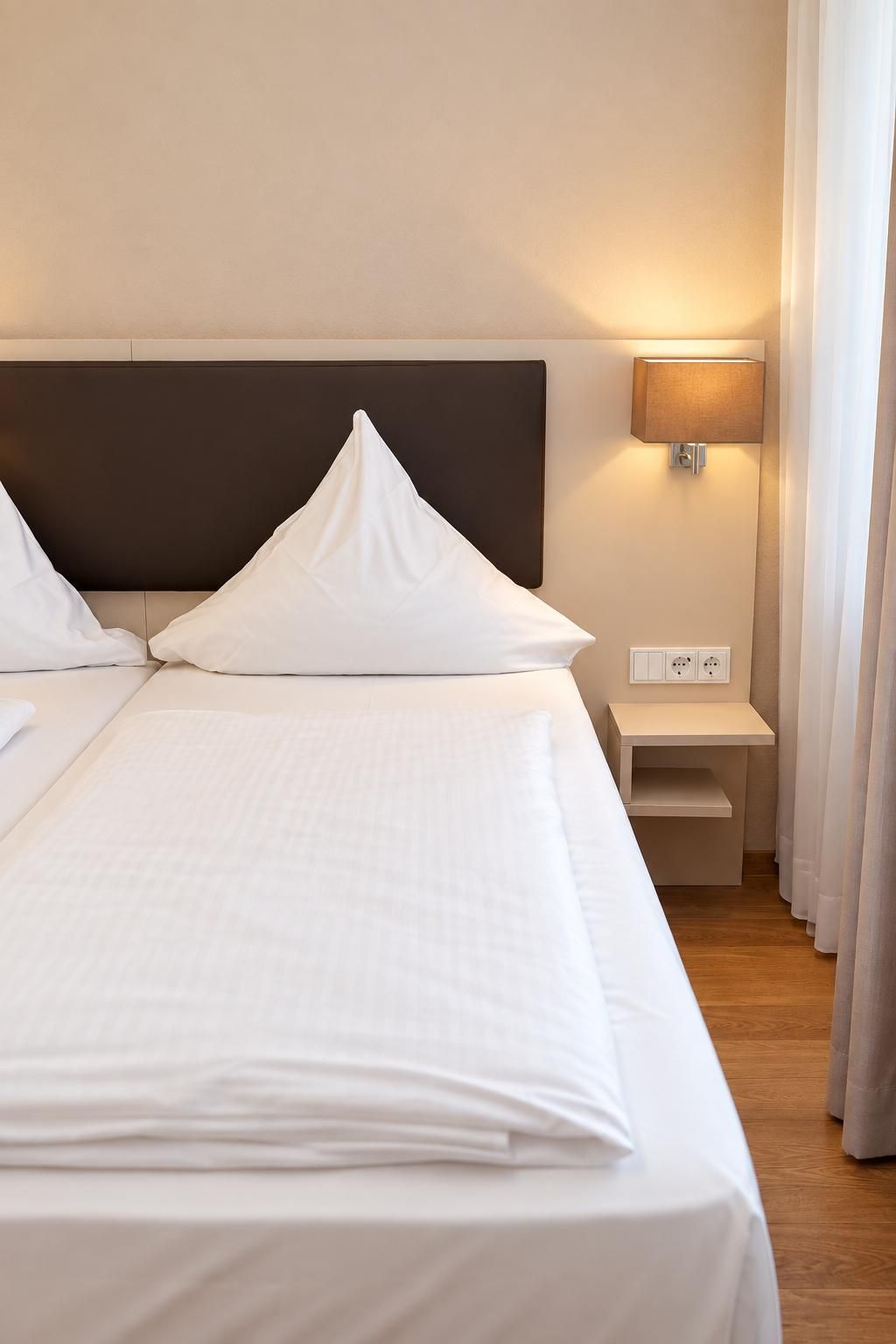 Ein Hotelzimmer mit einem großen Bett, einem Nachttisch, einer Lampe und einer Steckdose.
