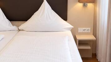 Ein Hotelzimmer mit einem großen Bett, einem Nachttisch, einer Lampe und einer Steckdose.