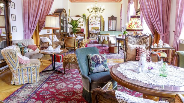 Ein wohnzimmer im Vintage-Stil mit einem großen, rot gemusterten Teppich, mehreren Sitzgruppen und klassischen Möbeln.