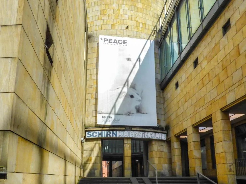 Un bâtiment sur lequel est accrochée une grande banderole faisant de la publicité pour « LA PAIX » et la « SCHIRN KUNSTHALLE ».