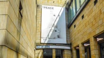 Un bâtiment sur lequel est accrochée une grande banderole faisant de la publicité pour « LA PAIX » et la « SCHIRN KUNSTHALLE ».