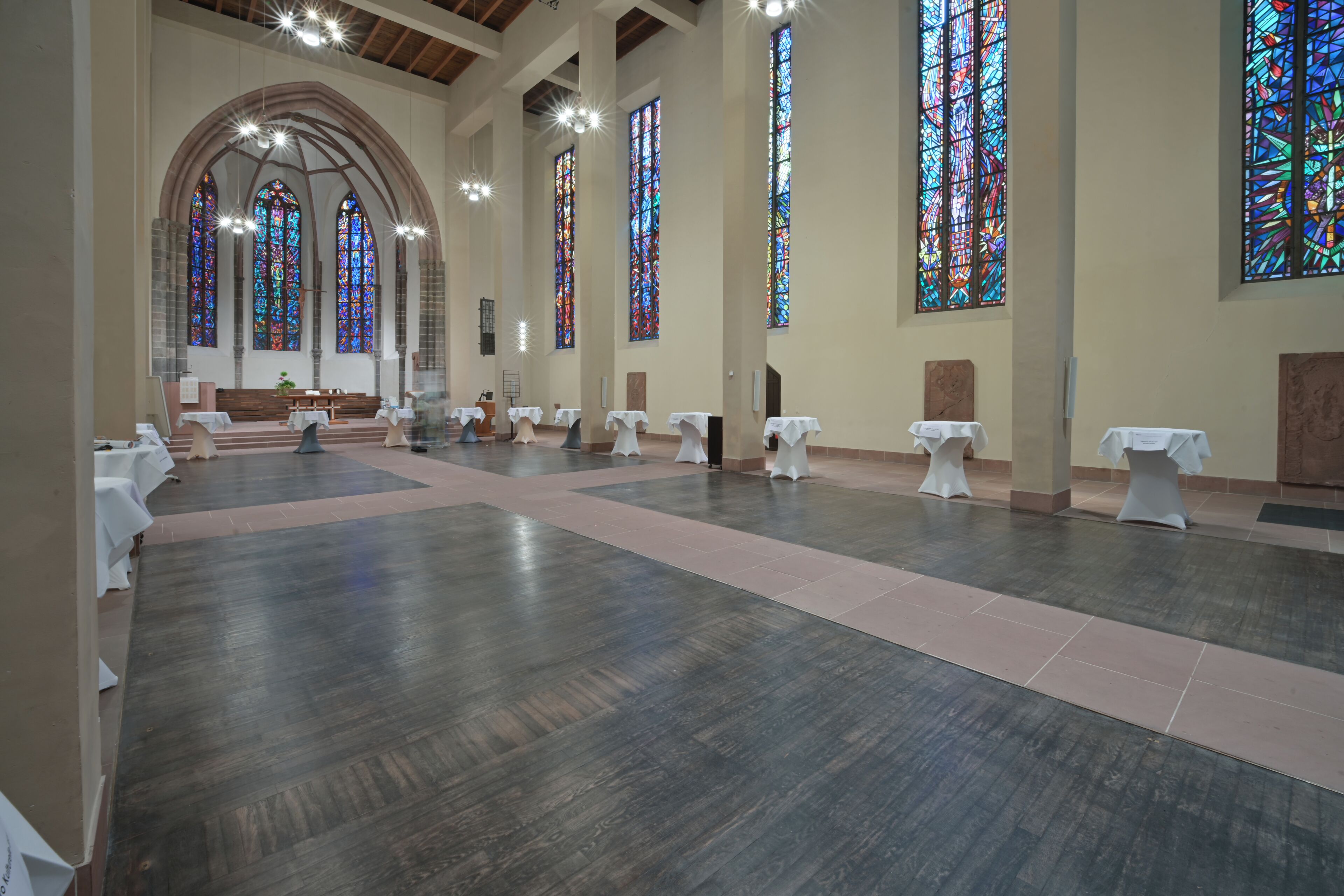 Un vaste hall doté de hauts plafonds, de grandes fenêtres à vitraux et de nombreuses tables disposées pour un événement.