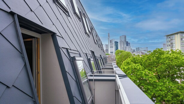 A modern building with a sloped roof, large windows, and a view of a cityscape.