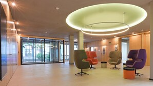 Moderni aula, jossa on lasinen sisäänkäynti, värikkäät tuolit ja ainutlaatuinen pyöreä kattovalaisin.