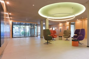 Een moderne lobby met een glazen ingang, kleurrijke stoelen en een bijzondere ronde plafondlamp.