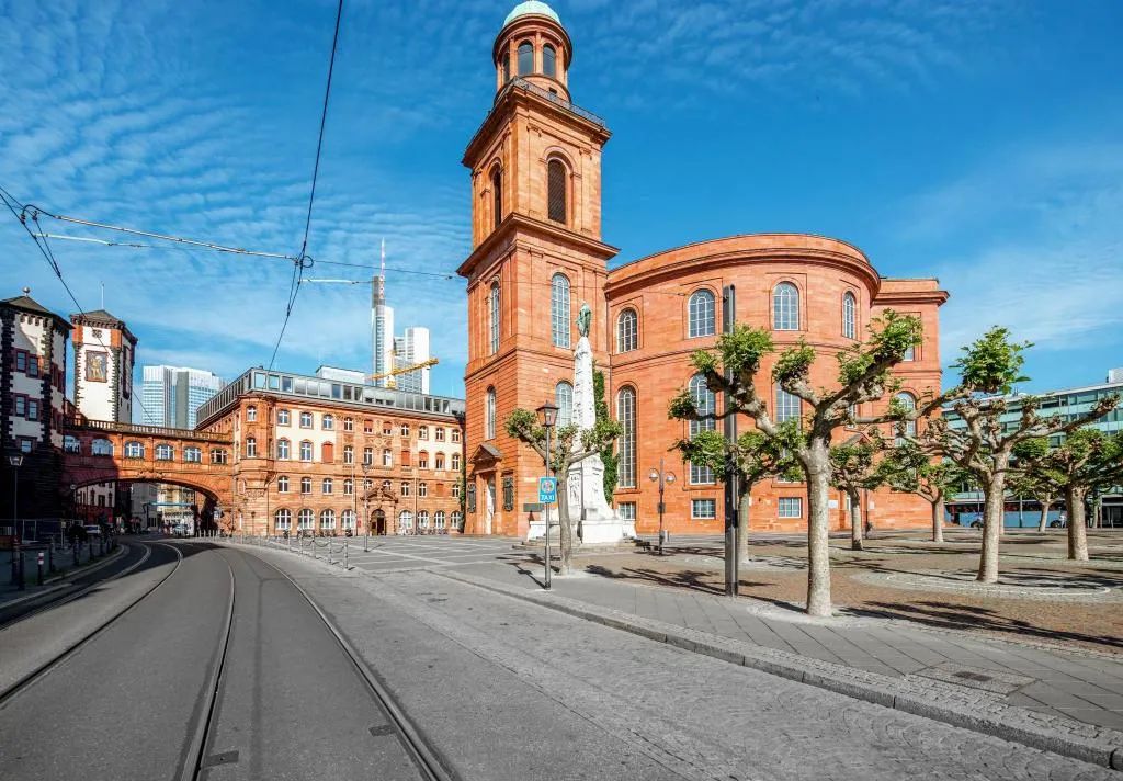 Una calle con vías de tranvía, un edificio de ladrillo rojo con una torre, y una estatua en primer plano.