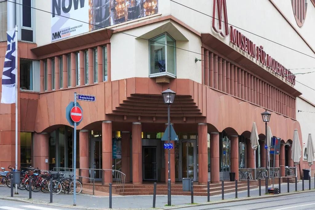 A building with a prominent 'Museum für Moderne Kunst' sign, a no-entry sign, and a row of bicycles parked outside.