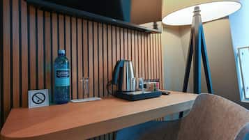 A hotel room with a wooden panel wall, a desk with a water bottle, a coffee maker, and a lamp.