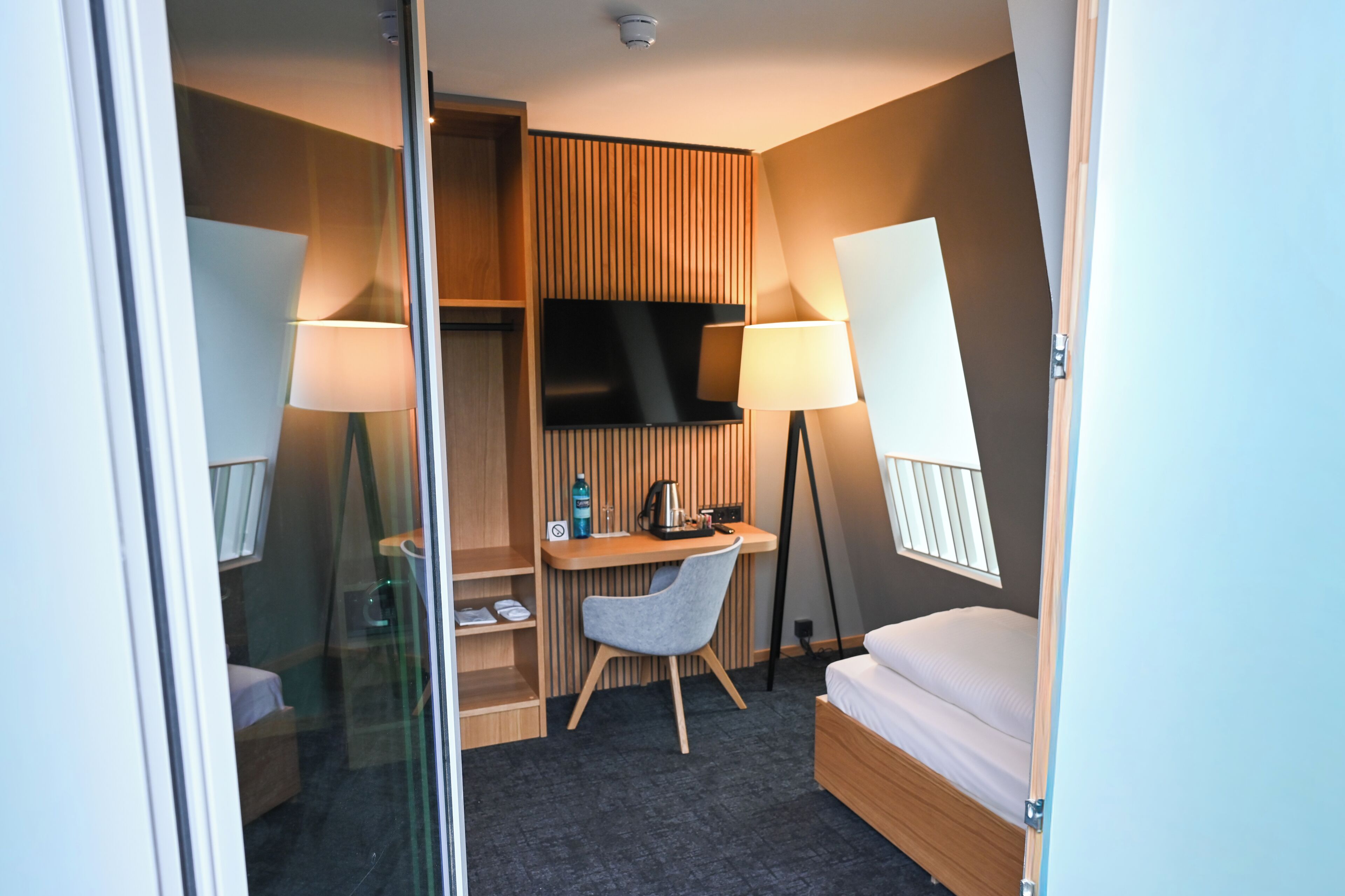 A hotel room with a bed, a desk with a chair, a television, and two lamps.
