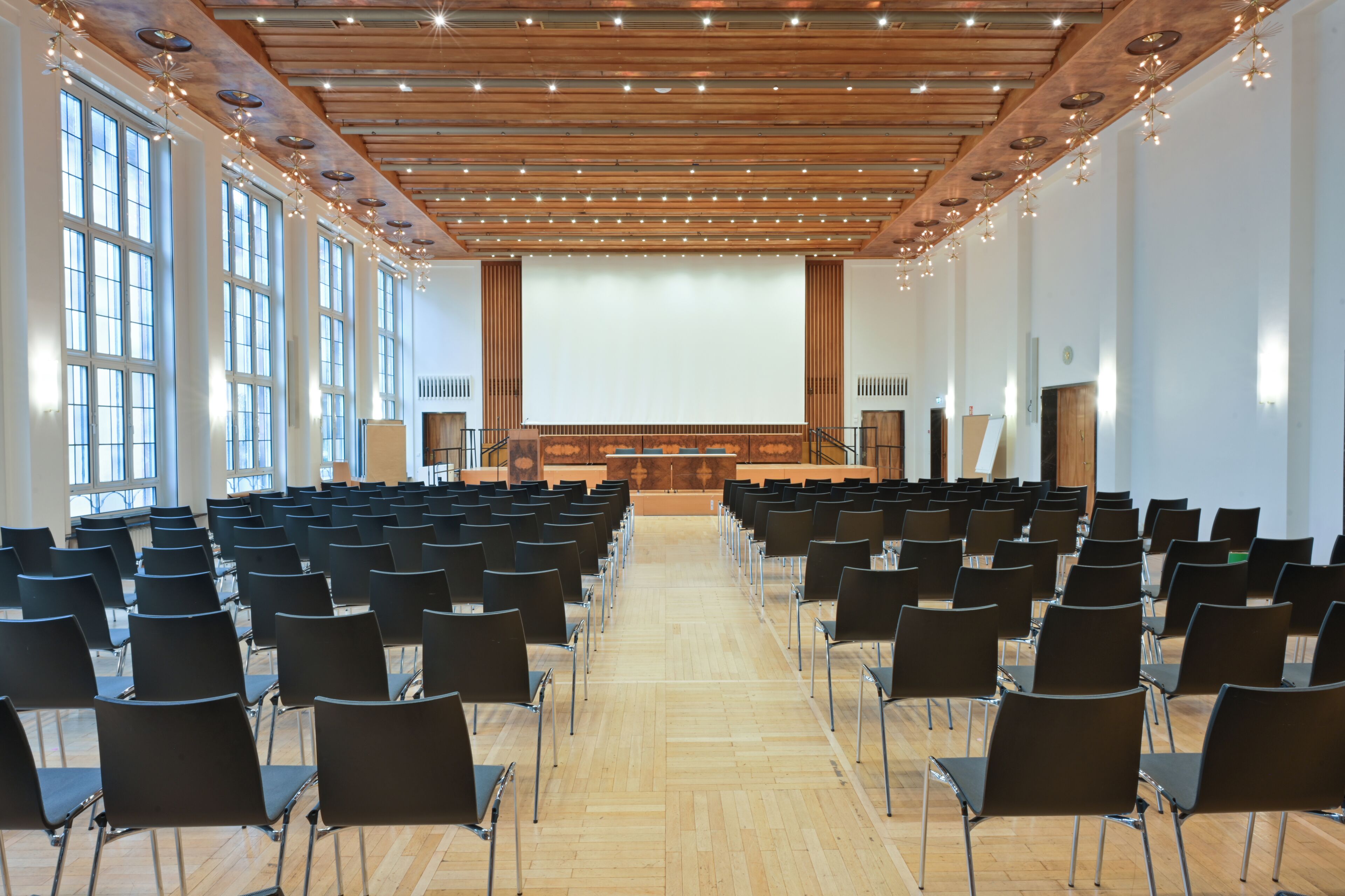 Un salón de conferencias con filas de sillas, techo de madera y ventanas amplias.