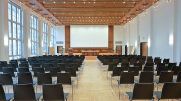 Un salón de conferencias con filas de sillas, techo de madera y ventanas amplias.