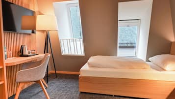 A hotel room with a bed, a desk, a chair, a TV, and two windows.