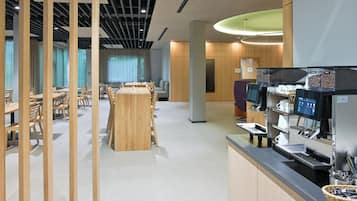 A modern cafe with wooden tables and chairs, a coffee machine, and a counter with a basket.