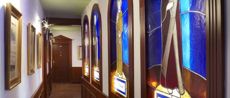 A hallway with wooden flooring, arched stained glass windows, and framed pictures on the walls.