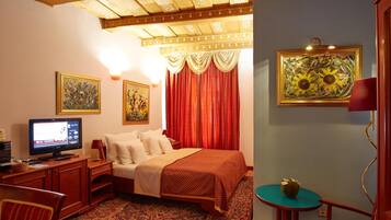 A hotel room with a bed, a desk with a computer, a television, a small table with a bowl, and two paintings on the wall.