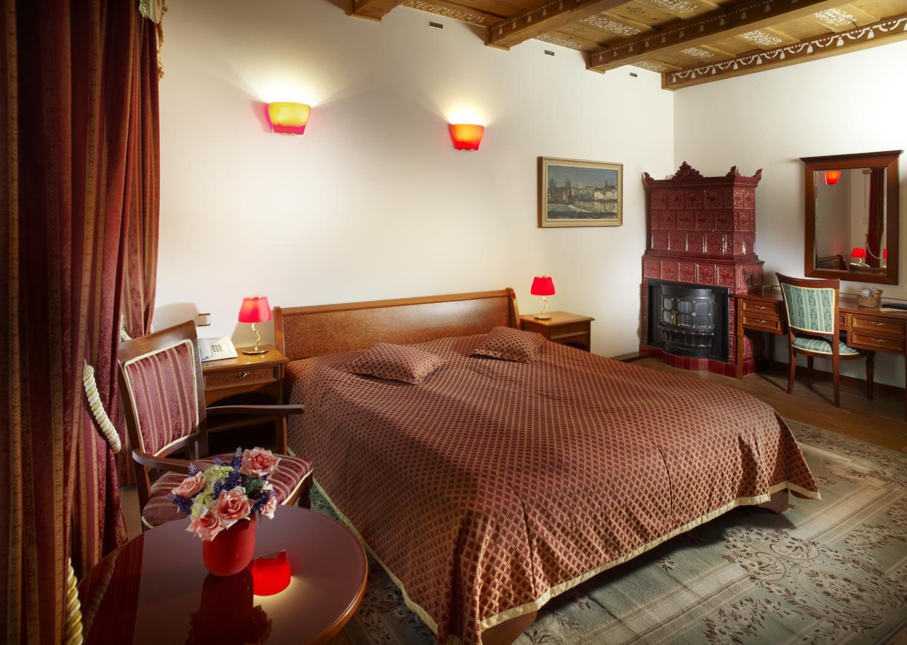 A bedroom with a large bed, two bedside tables with lamps, a wooden dresser, a mirror, and a fireplace.