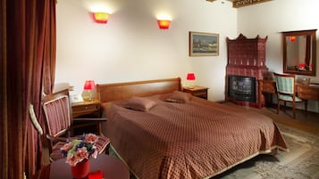 A bedroom with a large bed, two bedside tables with lamps, a wooden dresser, a mirror, and a fireplace.