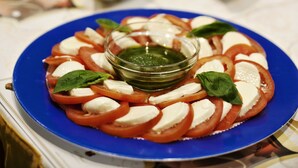 Pöydällä on useita erilaisia ruokia, muun muassa lautanen tomaatti-mozzarella-salaattia, joka on koristeltu basilikalla.