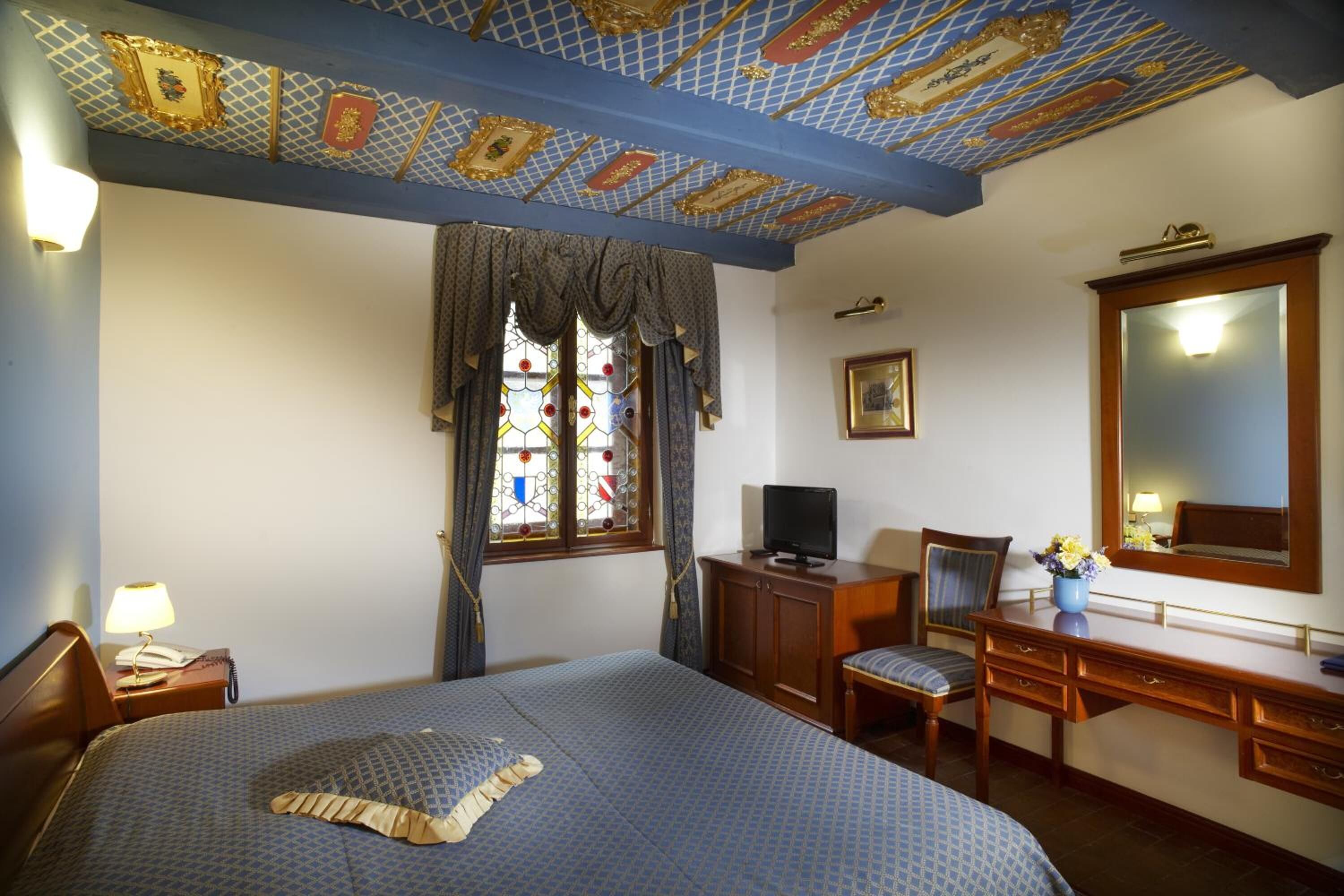 Habitación de hotel con una cama grande, un escritorio con silla, televisión y ventana con cortinas.
