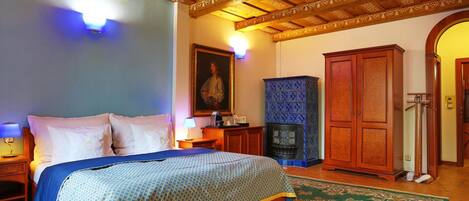 A bedroom with a bed, nightstands, a dresser, a fireplace, and a wooden ceiling.