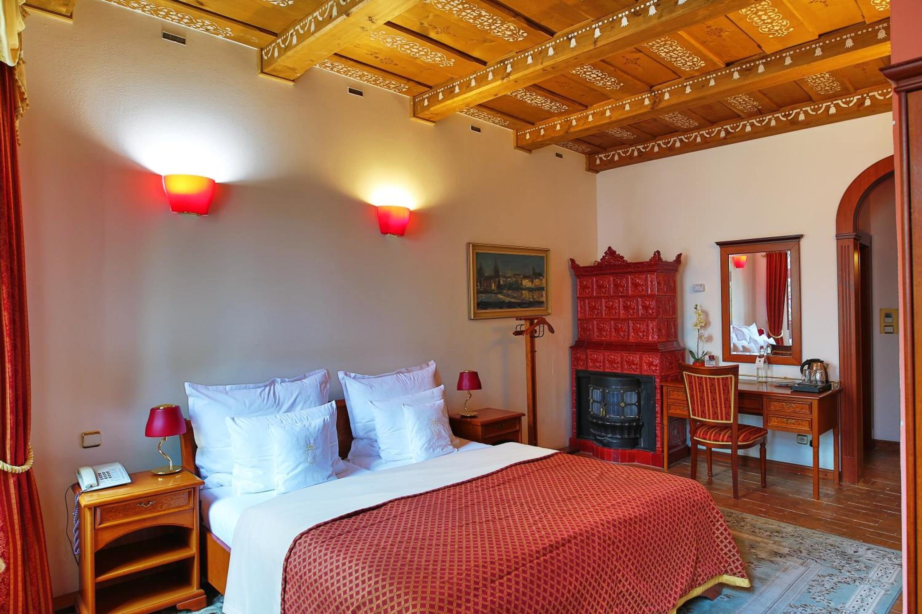 A hotel room with a bed, a desk, a chair, a fireplace, and a painting on the wall.