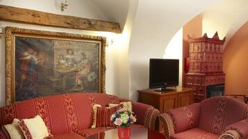 A traditional living room with patterned sofas, a central coffee table, a painting on the wall, and a television.