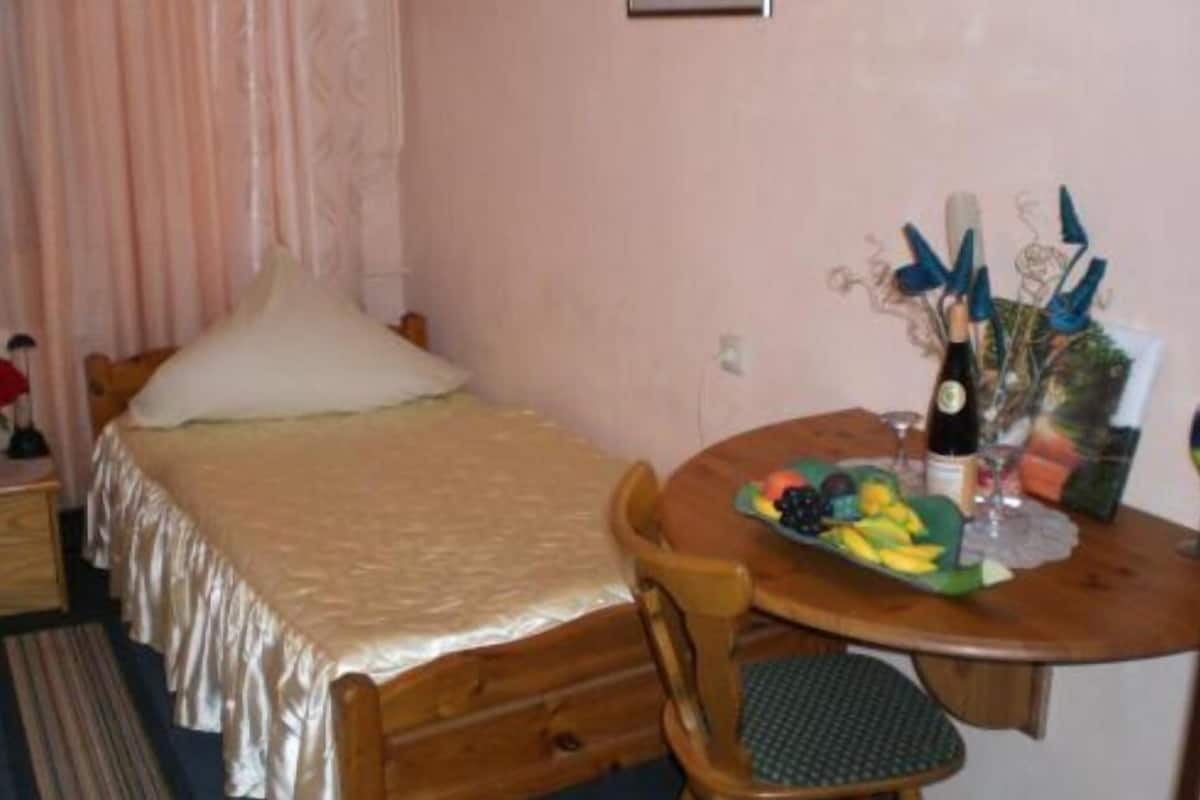A bedroom with a bed, a small table with a fruit bowl and a bottle, and a chair.