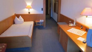A hotel room with a bed, bedside table, lamp, and a desk with a telephone and papers. - Godorfer Mühle (Cologne)