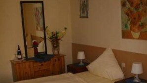 A hotel room with two beds, a wooden dresser, a mirror, and a painting on the wall. - Godorfer Mühle (Cologne)