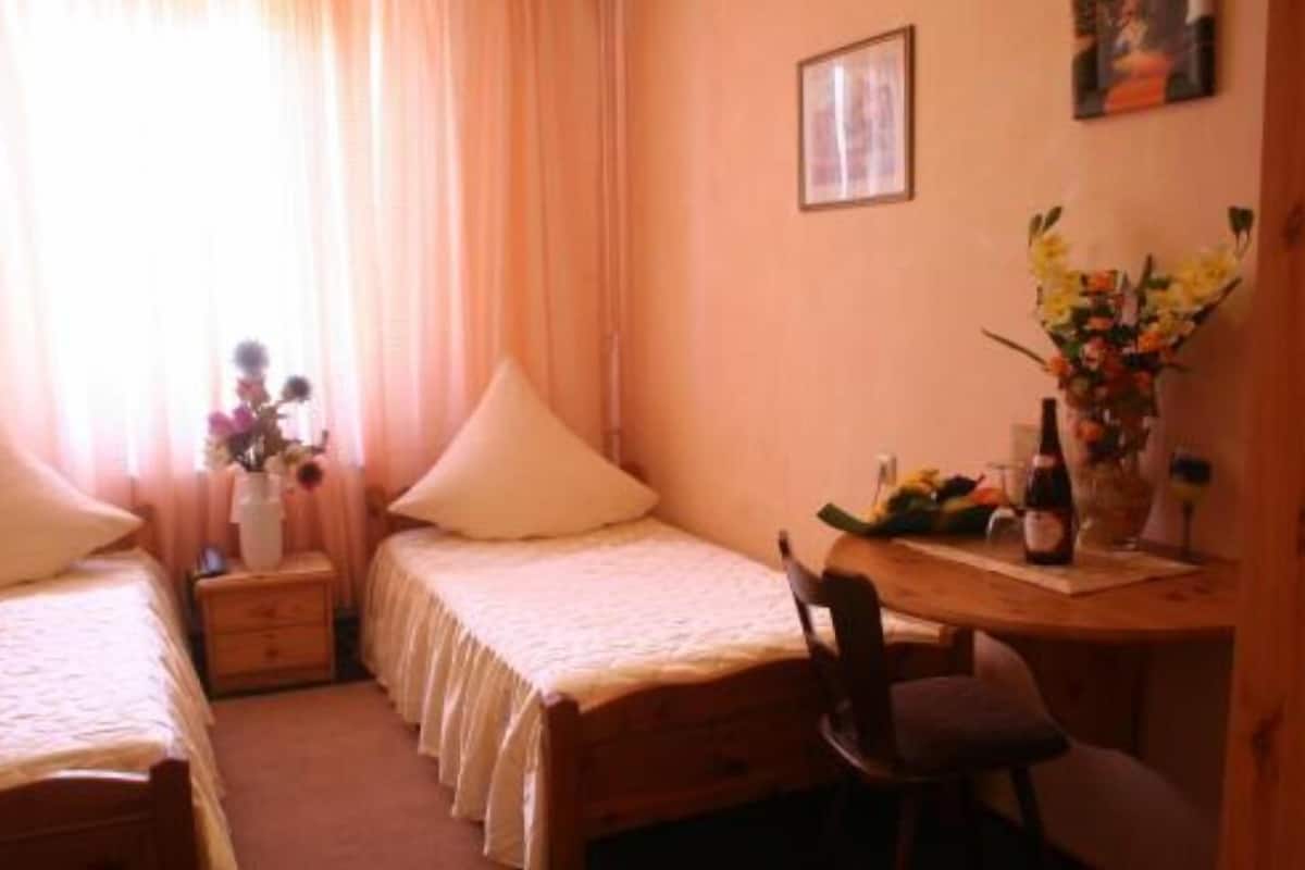 A bedroom with two beds, a wooden desk, a chair, a vase with flowers, and a framed picture on the wall.