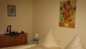 A hotel room with a bed, a dresser, a lamp, and a painting on the wall. - Godorfer Mühle (Cologne)