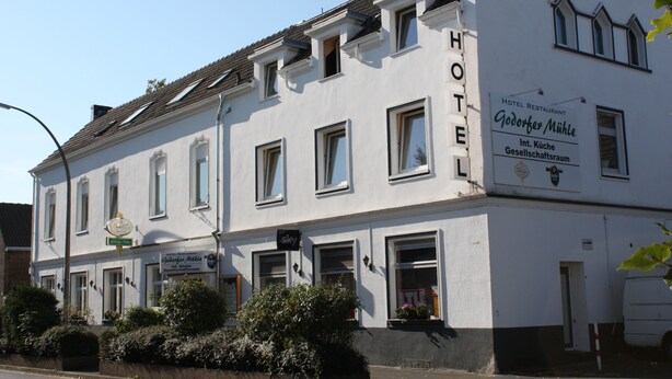 A white building with a sign indicating it is a hotel. There are multiple windows, some with curtains, and a small balcony area. - Godorfer Mühle (Cologne)