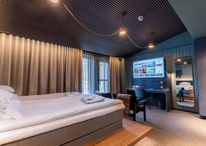 Moderni hotellihuone, jossa on suuri sänky, työpöytä ja televisio, jonka näytöllä näkyy matkanvarauspalvelun verkkosivusto.