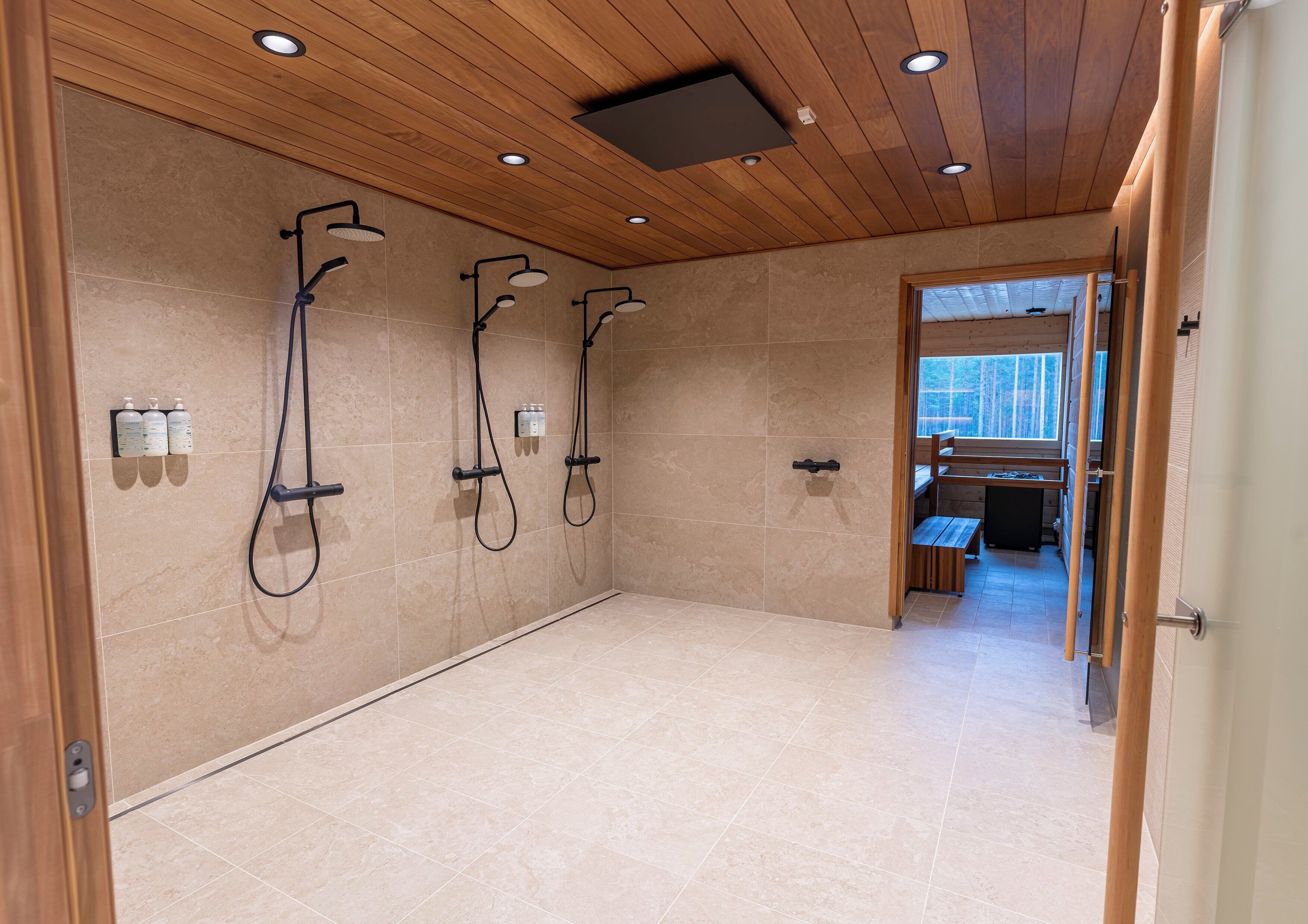 A modern bathroom with three showerheads, a wooden ceiling, and a view into a dining area.