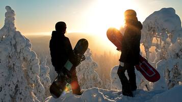 Two people holding snowboards on a snowy mountain with the sun in the background.