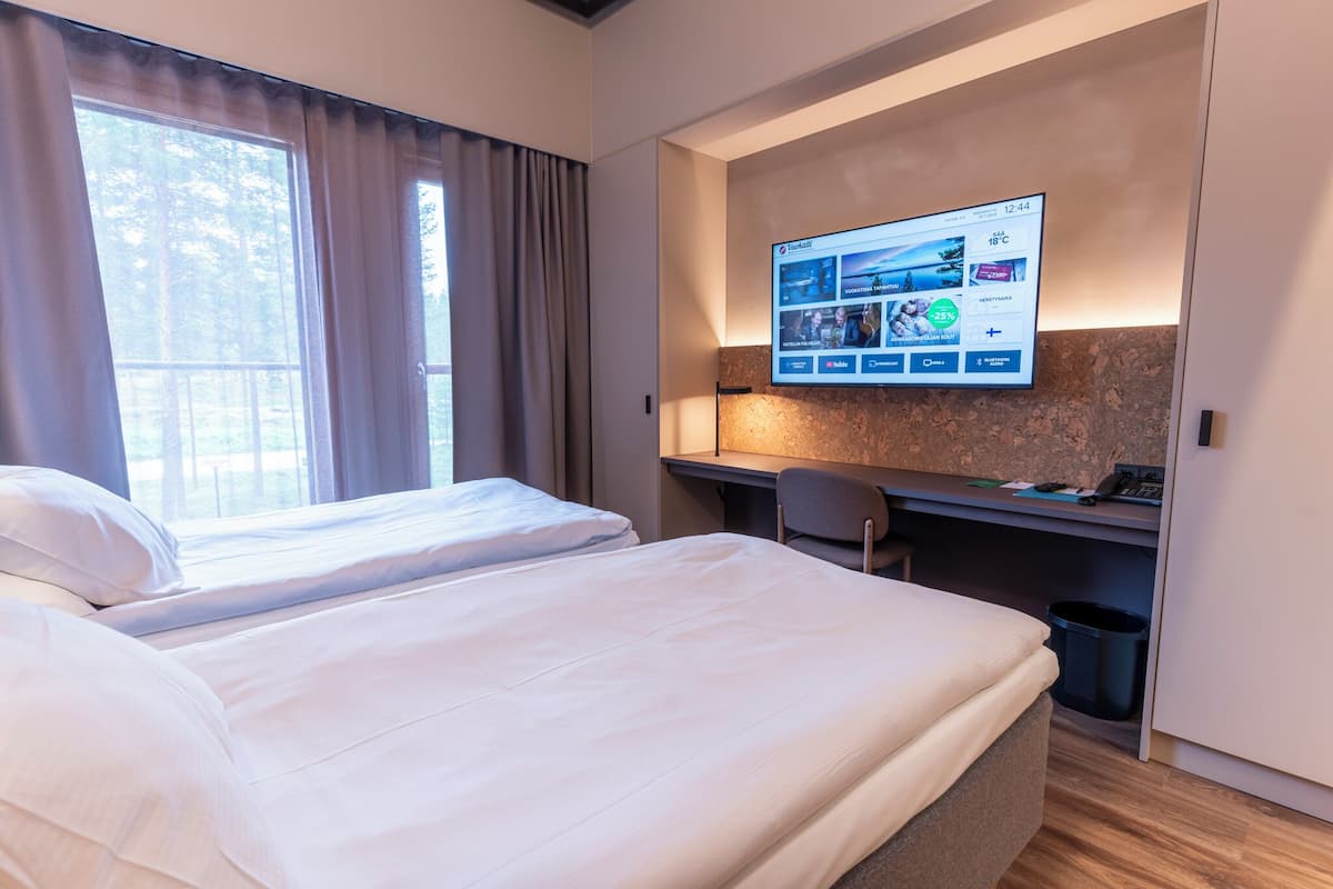A hotel room with a bed, a desk, and a TV mounted on the wall displaying a weather app.