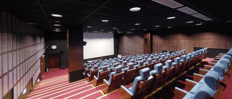 A theater with rows of wooden seats, a red carpeted floor, and a large screen at the front.
