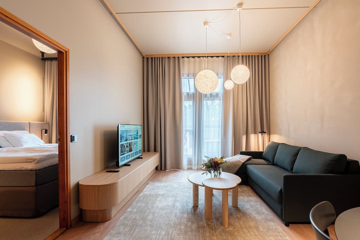 A modern hotel room with a bed, a TV, a sofa, a coffee table, and a small side table.