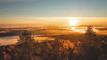 Metsäinen maisema, jonka yllä auringonnousu heijastuu vesistöstä.