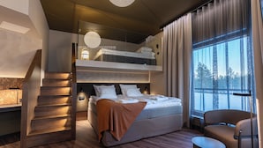 Een moderne hotelkamer met een stapelbed, een houten trap, een zithoek en een groot raam met uitzicht op bomen.