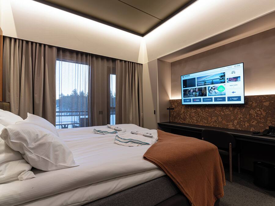 Habitación de hotel con cama, escritorio, televisor montado en la pared y ventana con cortinas.
