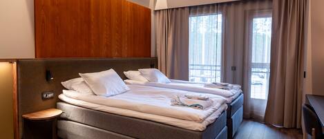 A modern hotel room with a large bed, a bedside table, and a view of the outdoors through the window.