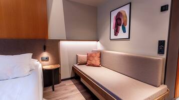A modern hotel room with a bed, a sofa, a small side table, and a wall-mounted light.