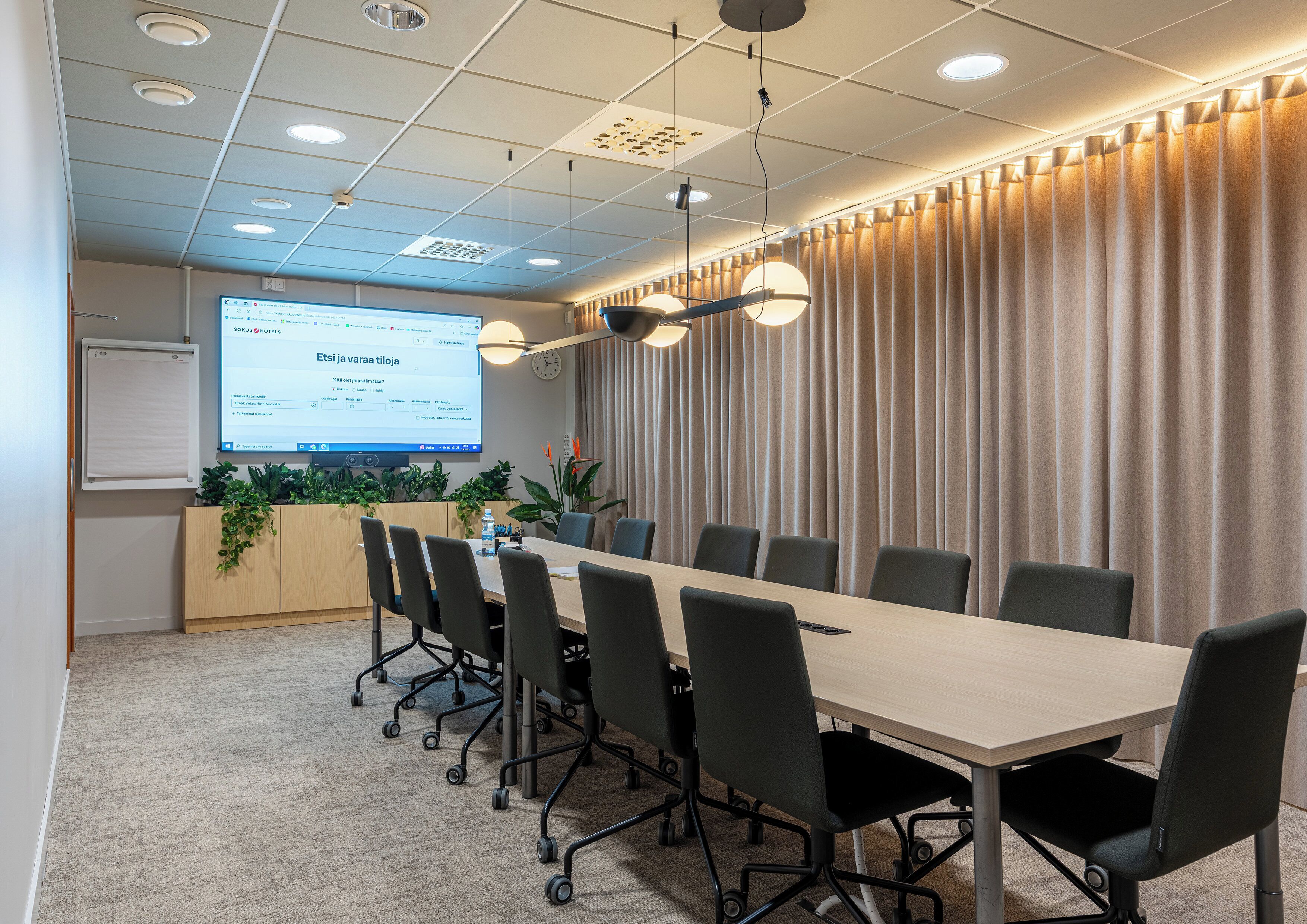 A conference room with a long table, chairs, a projector screen, and a curtain backdrop.